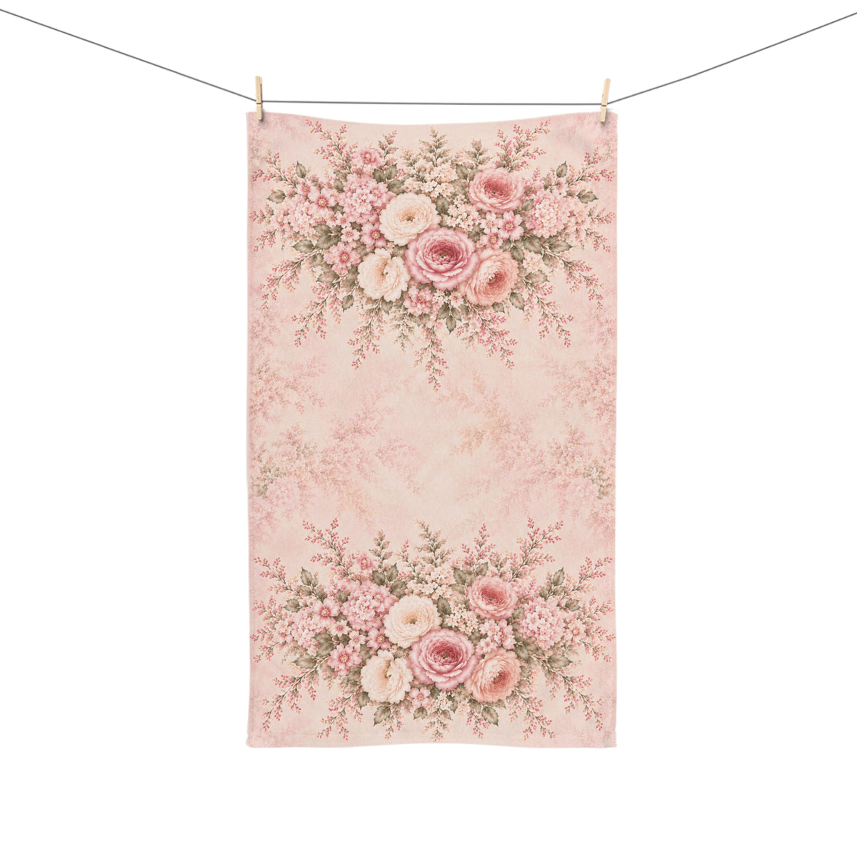 A rectangular fabric hand towel or tea towel with a vintage floral toile pattern in shades of pink, beige, and green, hanging from two wooden clothespins on a white string against a solid white background.