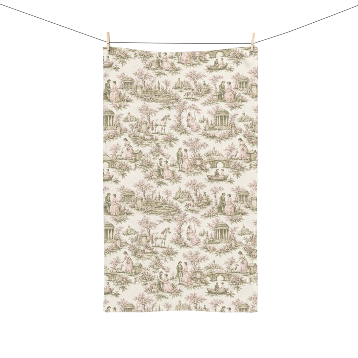 A rectangular hand or tea towel featuring a classic French toile de Jouy pattern with figures, trees, and classical architecture in muted pink and sage green on an off-white background, hanging from a clothesline with wooden clips.